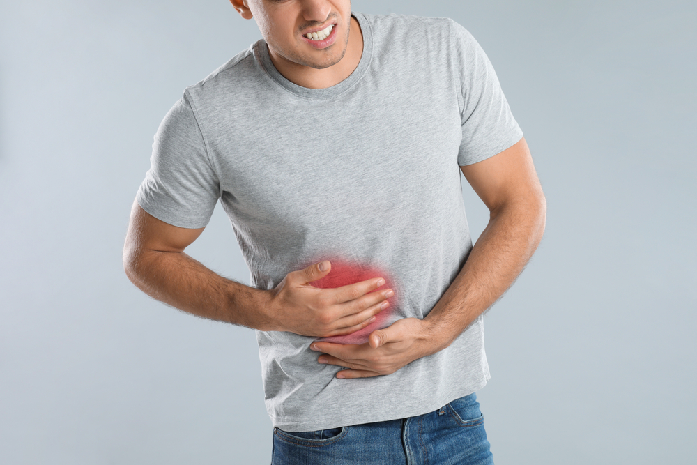 A man suffering from liver pain on a grey background.