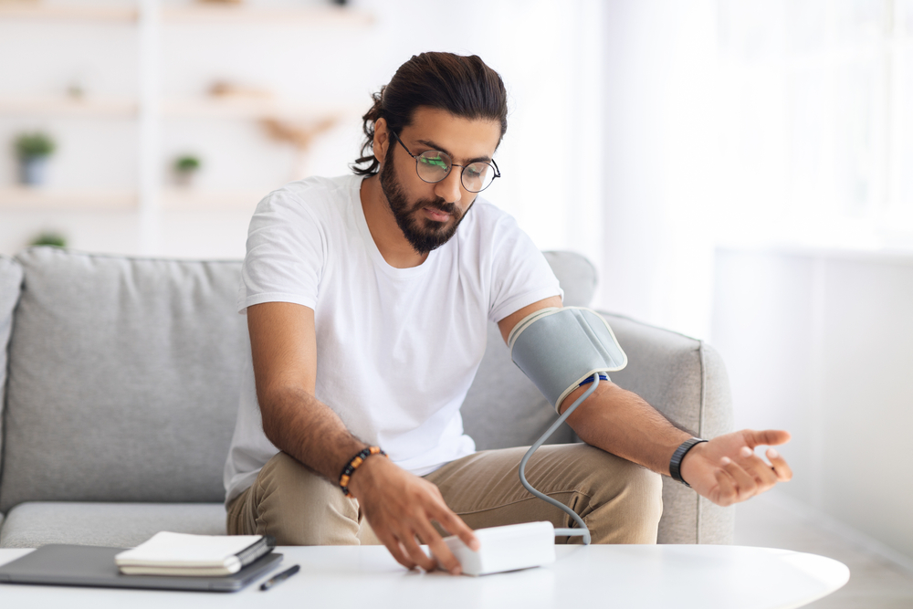 A young arab man on a couch checking on his blood pressure.