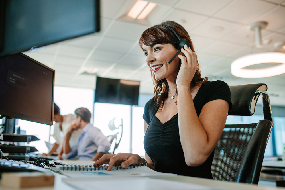 A woman on a headset is talking while looking at a computer screen.